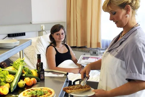 Verpleegkundige serveert een maaltijd aan een patiënt in een ziekenhuisbed
